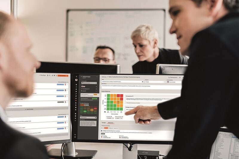 Im Büro: Ein Kollege deutet auf eineBildschirm, auf dem Analysedaten zu sehen sind.