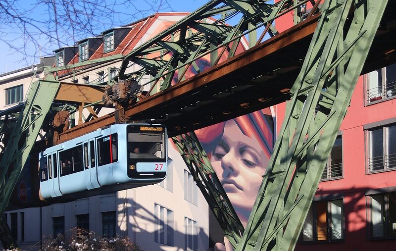 Die Schwebebahn fährt an einem großen Mural vorbei. Das Wandbild zeigt das Gesicht einer Frau.