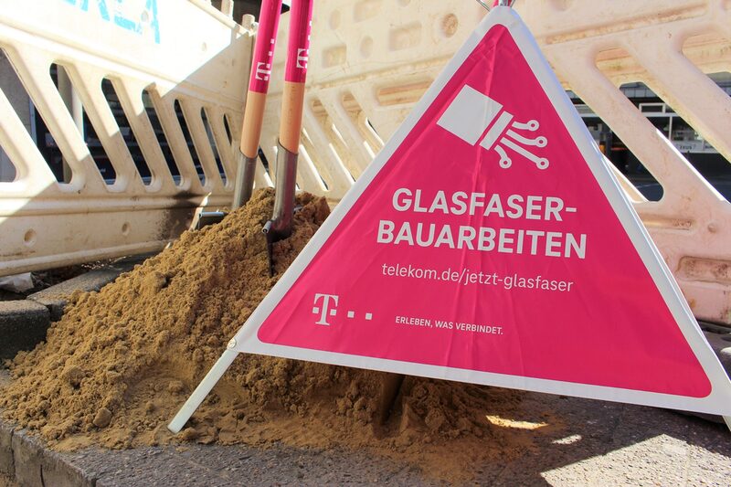 Baustelle auf dem Gehweg mit einem aufgestellten Infoschild der Telekom davor.